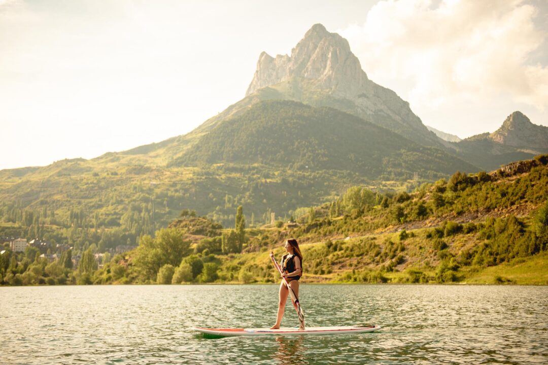 Mujer practicando paddle surf en un lago con el pico Midi d’Ossau al fondo.
