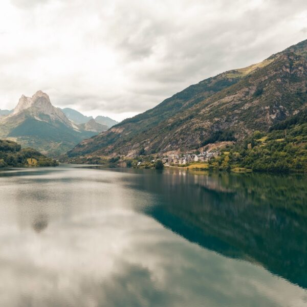 Lago de Lanuza con el monte reflejado en el agua y el pueblo al fondo.